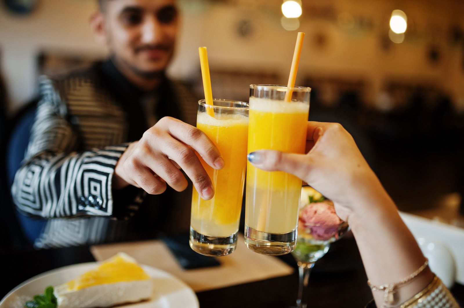 Close up hands of lovely indian couple in love, sitting on restaurant and cheers together by orange juice.